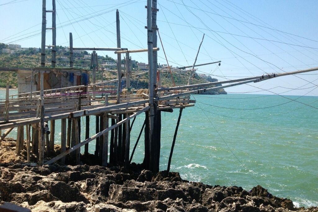 A pier with a wooden structure extending into the water, surrounded by rocky terrain and a hillside in the background.