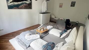 Un dormitorio moderno con una cama grande, una mesita con juego de té, un sofá, una mesita de noche, un reloj de pared y un cuadro de un paisaje costero.