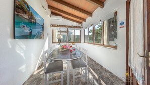 Un coin repas avec une table ronde, des chaises blanches et un tableau représentant un bateau accroché au mur.