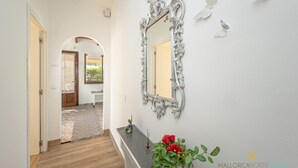 Un couloir doté d’un plancher en bois, d’un mur blanc, d’un miroir décoratif et d’une plante en pot ornée de fleurs rouges.