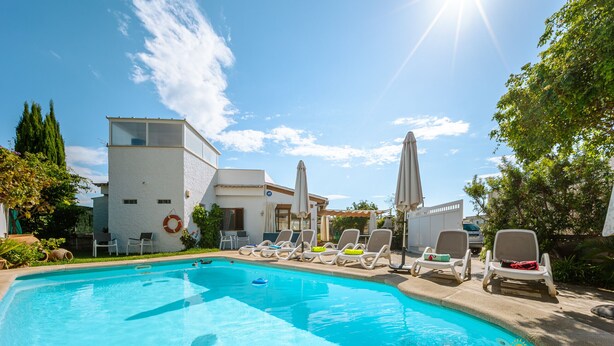 Une piscine entourée de bâtiments et de verdure, avec des chaises longues et des parasols.