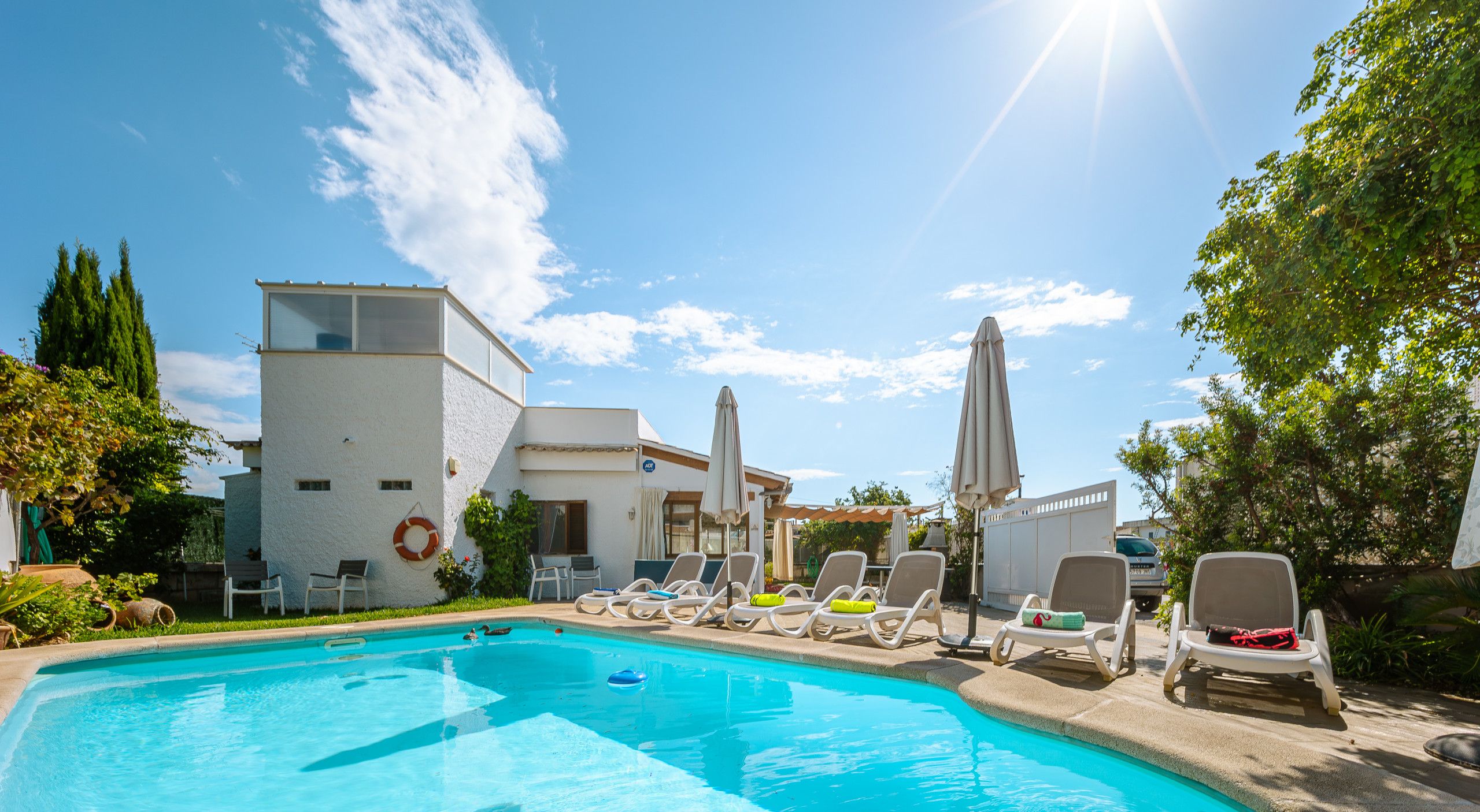 A swimming pool with lounge chairs and umbrellas, surrounded by buildings and greenery.