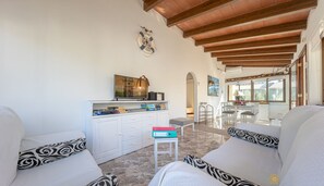 Un amplio salón con techo alto, muebles blancos y un televisor sobre un mueble blanco.