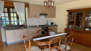 A kitchen with wooden cabinets, a dining table with chairs, a microwave, and a cabinet with glass doors. - Carpenter's house (Crecente)