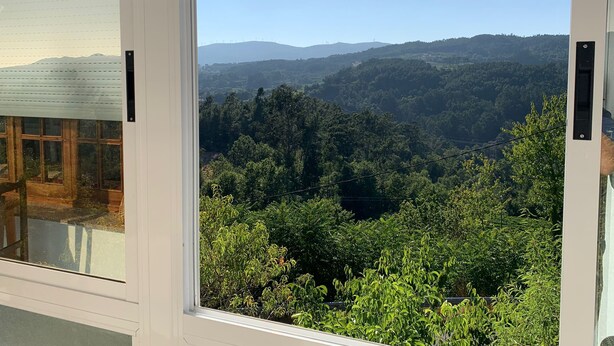 A view from a window overlooking a forested valley with distant mountains. - Carpenter's house (Crecente)
