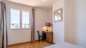 Une chambre à coucher avec un lit, un bureau, une chaise, une fenêtre avec des rideaux et un miroir sur le mur.