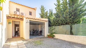Un bâtiment avec une porte de garage ouverte, un vélo garé à l’extérieur et une allée gravillonnée.