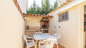 Une terrasse avec une table et des chaises, un four en briques et une porte blanche.