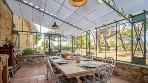 Un área de comedor al aire libre cubierta con una mesa dispuesta para cuatro personas, rodeada de muros de piedra y amplias ventanas.