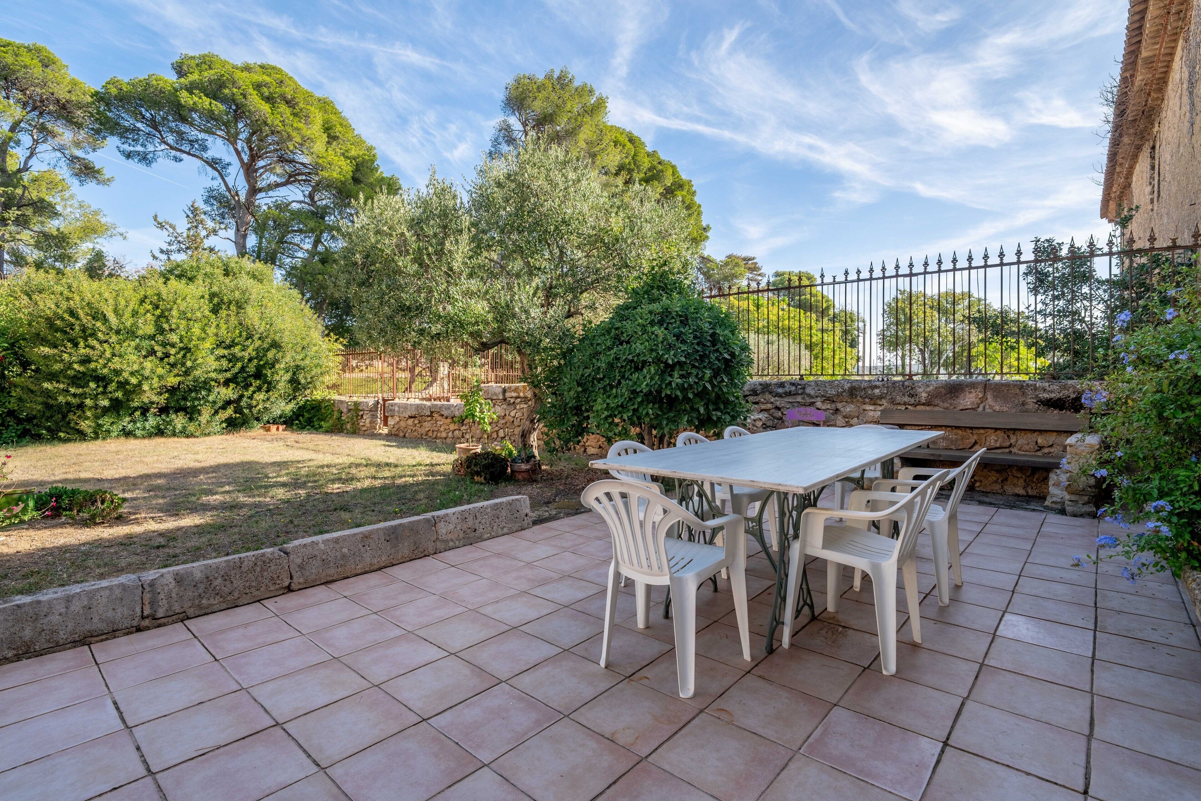 A patio with a table and chairs, surrounded by greenery and a stone wall.