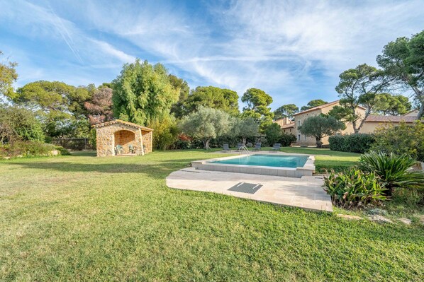 A backyard with a swimming pool, a stone gazebo, and surrounding greenery.