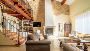 Amplio salón con pared de piedra, escalera de madera y chimenea.