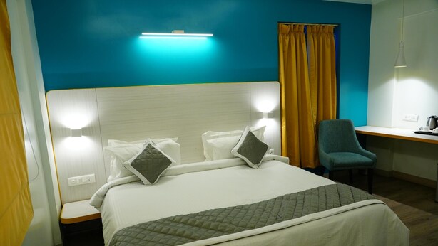 A hotel room with a bed, bedside lamps, a desk, and a chair. - SLR Residency (Bengaluru)