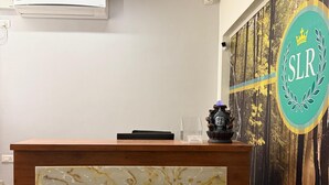 A reception desk with a marble-like panel, a logo on the wall, and a plant in the foreground. - SLR Residency (Bengaluru)