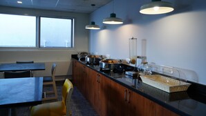 A kitchen area with a long counter, multiple stainless steel appliances, and hanging pendant lights. - SLR Residency (Bengaluru)