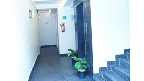A hallway with a fire extinguisher, a sign indicating a women's restroom, and a staircase leading to an upper floor. - SLR Residency (Bengaluru)