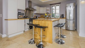 A modern kitchen with white cabinets, a stainless steel range hood, a central island with bar stools, and a built-in refrigerator. - Rosepeche, a beautiful villa with a castle feel (Les Eyzies)