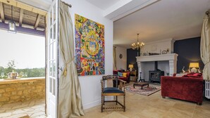 A spacious living room with a fireplace, a large colorful painting, and a view of the outdoors. - Rosepeche, a beautiful villa with a castle feel (Les Eyzies)