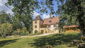 A traditional stone building with a steep roof, a central tower, and a covered wooden structure storing firewood. - Rosepeche, a beautiful villa with a castle feel (Les Eyzies)