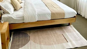 A neatly made bed with a wooden headboard, a patterned rug, and sheer curtains on a window. - Peaceful 2BHK Retreat | Near Forest Reserve (Kathmandu)