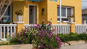 En gul bygning med en hvid veranda, plantekasser og mange blomster.