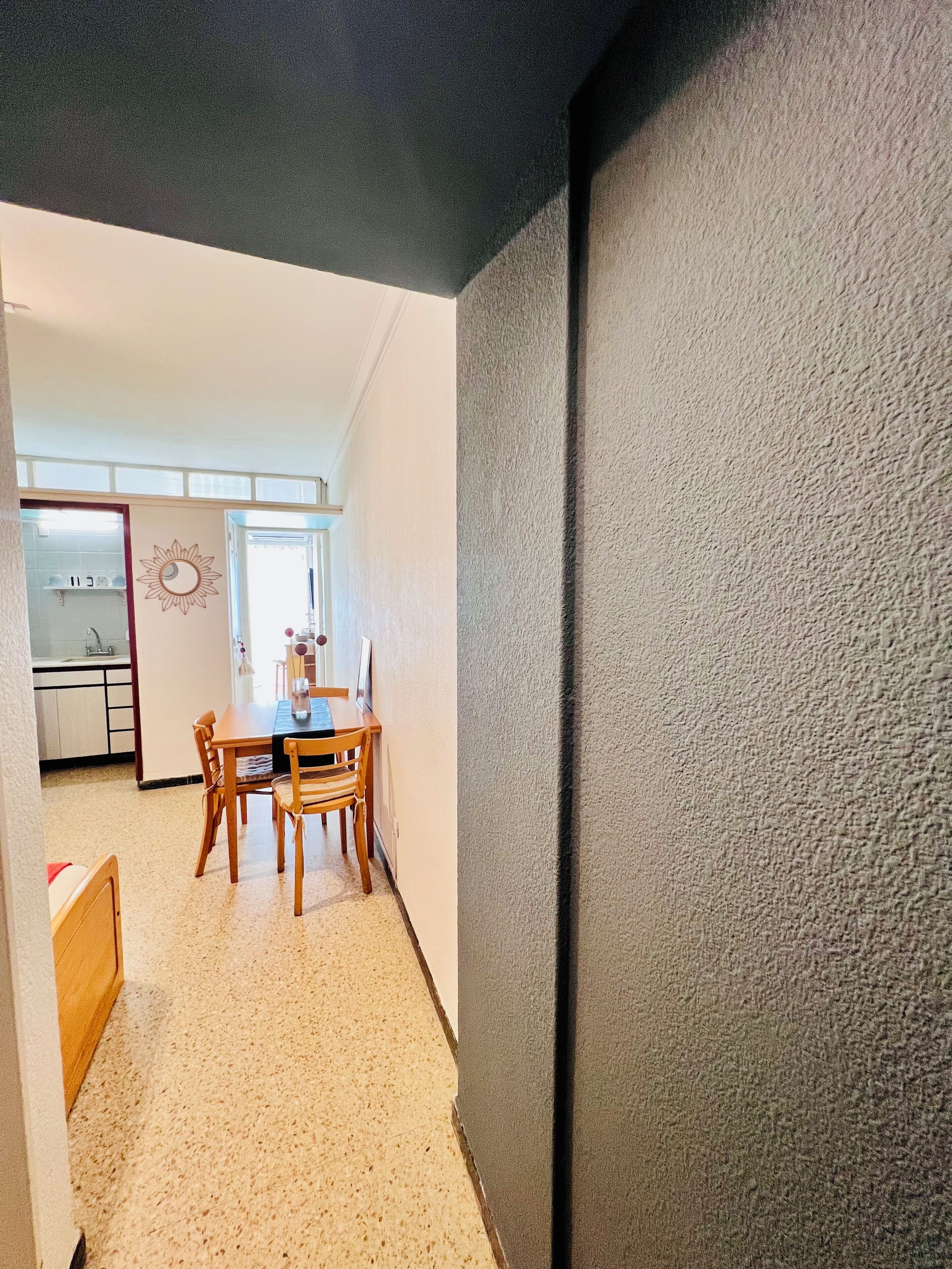Un pasillo que conduce a un comedor con una mesa y sillas, una cocina al fondo y una pared texturizada a la derecha.