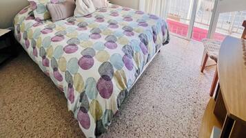 Un dormitorio con cama, un colgador de macramé, una ventana con cortinas y vistas a edificios.