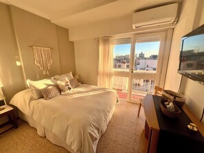 Ein Hotelzimmer mit Bett, Schreibtisch, Fernseher und einem Balkon mit Blick auf die Stadt.