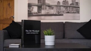 Een zwart gastenboek met de titel 'The Old Woodyard' op een tafel, met een kleine potplant naast een grijze bank.