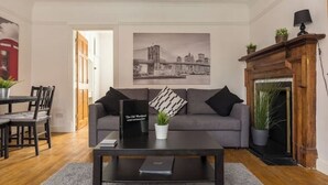 Een woonkamer met een bank, een salontafel, een open haard en een stadslandschap op de muur.
