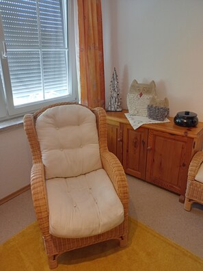 Una silla de mimbre con asiento y respaldo acolchados, sobre una alfombra amarilla.