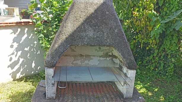 A stone-built outdoor oven with a metal rack, surrounded by grass and a concrete base. - Cozy and large vacation apartment on the Nömerberg (Windorf)