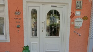 A house with a two-door entrance, a green gas cylinder, a red and yellow doormat, and a stone-paved entrance. - Cozy and large vacation apartment on the Nömerberg (Windorf)