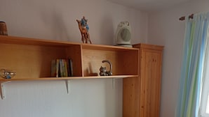 A single bed with a wooden frame, a bedside table with a lamp, and a shelf with a fan and a figurine. - Cozy and large vacation apartment on the Nömerberg (Windorf)