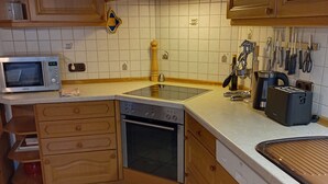 A kitchen with wooden cabinets, a microwave, an oven, a sink, and various kitchen utensils. - Cozy and large vacation apartment on the Nömerberg (Windorf)
