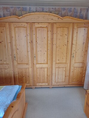 Ein Zimmer mit einem großen Holzschrank, einem Bett mit gemustertem Überwurf und einem strukturierten Boden.
