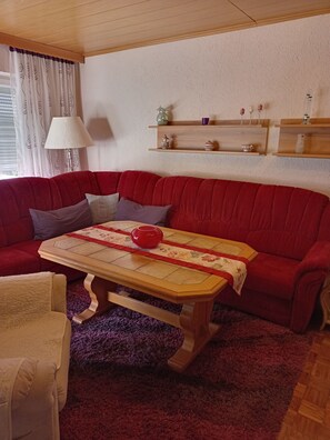 Un salon avec un canapé rouge, une table basse en bois, une lampe et des objets décoratifs disposés sur des étagères.