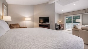 A hotel room with a large bed, a television, a desk with a chair, and a balcony with a view.