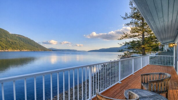 A wooden deck with a railing overlooking a calm lake, surrounded by hills.