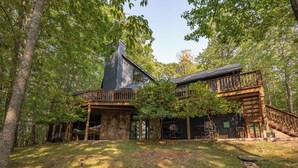 A rustic cabin with a stone foundation, wooden deck, and a chimney.