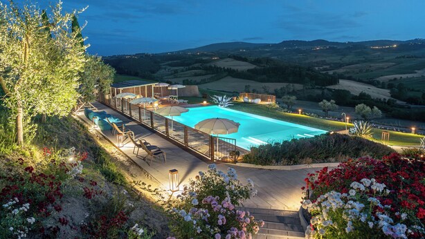 Zona de piscina con vistas al campo, rodeada por una terraza de madera y mobiliario exterior.