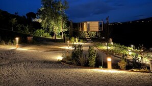 Una casa moderna con camino de entrada de grava, rodeada de árboles y una colina al fondo.