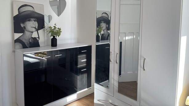 Een kamer met een witte kast, een zwarte kast met lades, een spiegel en een lijst met een afbeelding aan de muur.