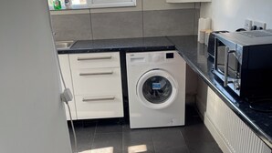 Een praktische keuken met een wasmachine, een magnetron en een raam dat natuurlijk licht binnenlaat.