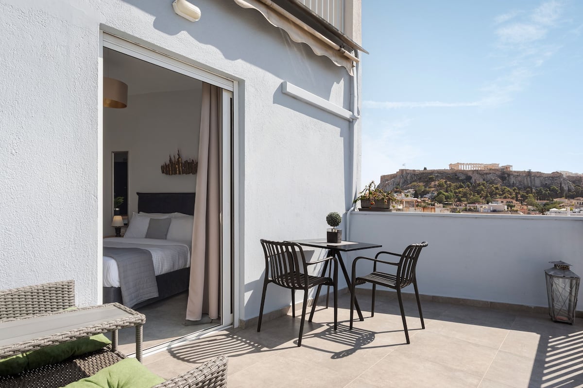 A balcony with a bed, a table with chairs, and a view of a historical site in the distance.