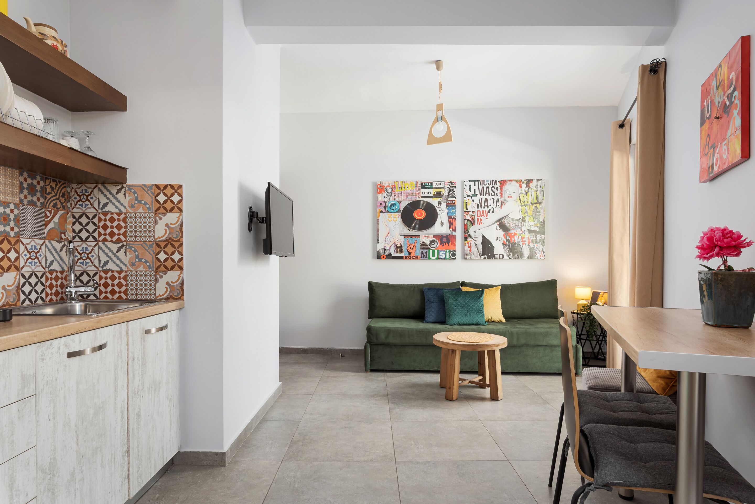 Ein kompakter Wohnbereich mit Küchenzeile, einem grünen Sofa, einem kleinen runden Tisch und einem an der Wand befestigten Fernseher.