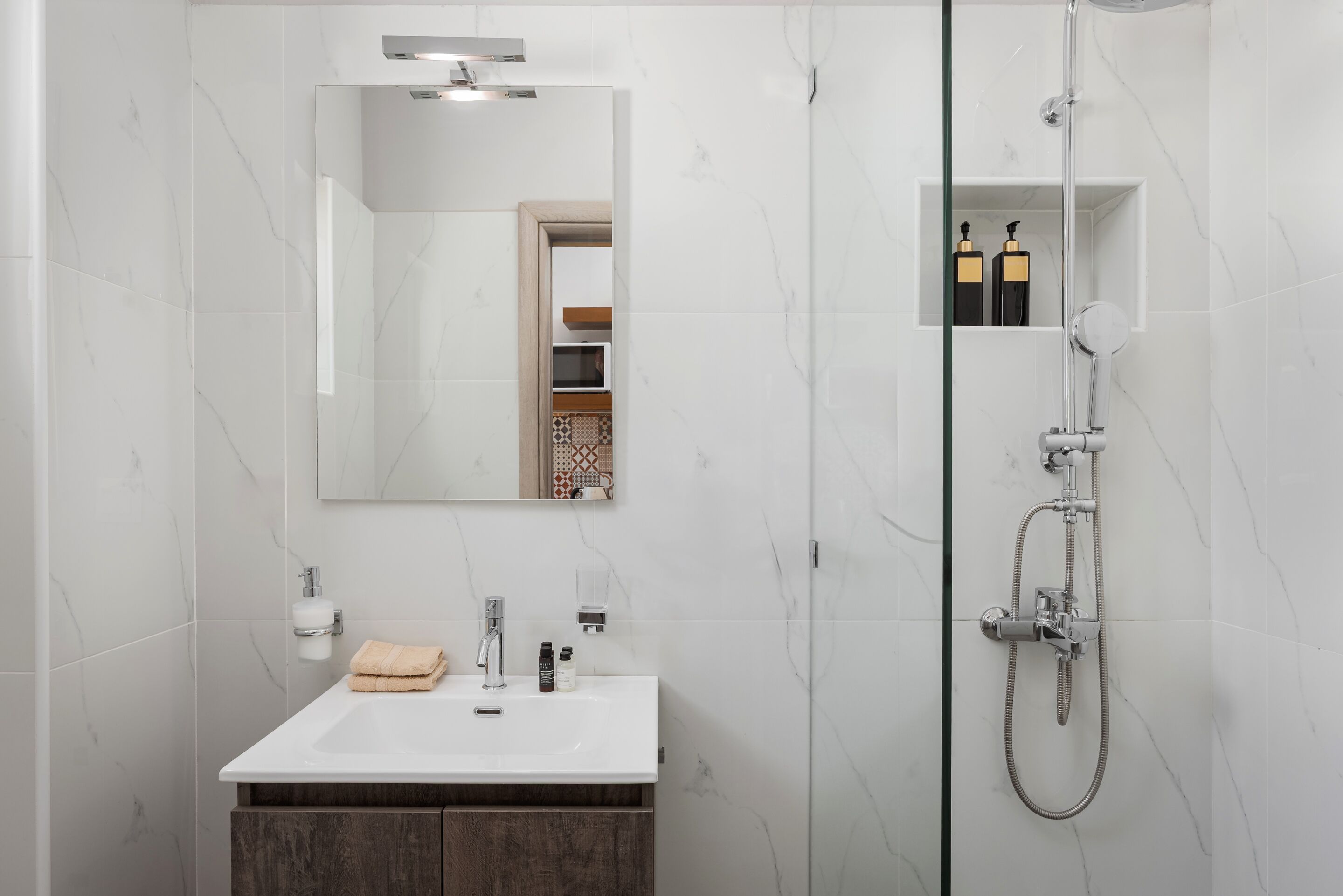 Ein modernes Badezimmer mit einem weißen Marmorwaschbecken, einer Duschkabine aus Glas und einem Spiegel über dem Waschbecken.