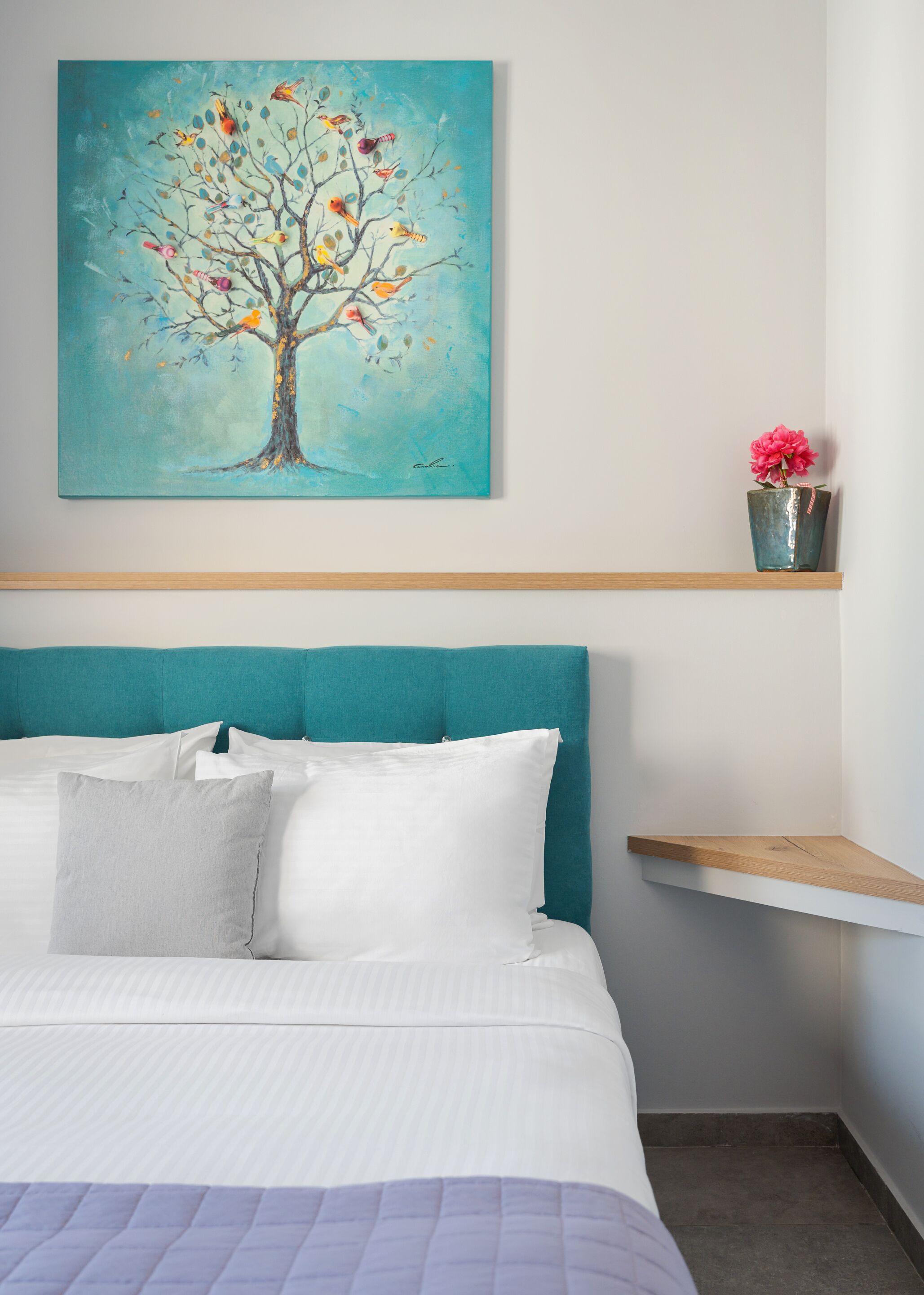 Una camera da letto con una testiera color petrolio, un letto con biancheria bianca, una parete color petrolio e un quadro raffigurante un albero con degli uccelli.