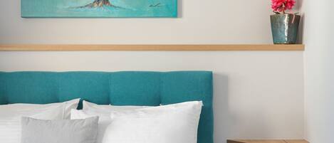 Una camera da letto con una testiera color petrolio, un letto con biancheria bianca, una parete color petrolio e un quadro raffigurante un albero con degli uccelli.