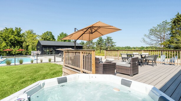 Un jacuzzi en una terraza de madera, con una piscina al fondo.